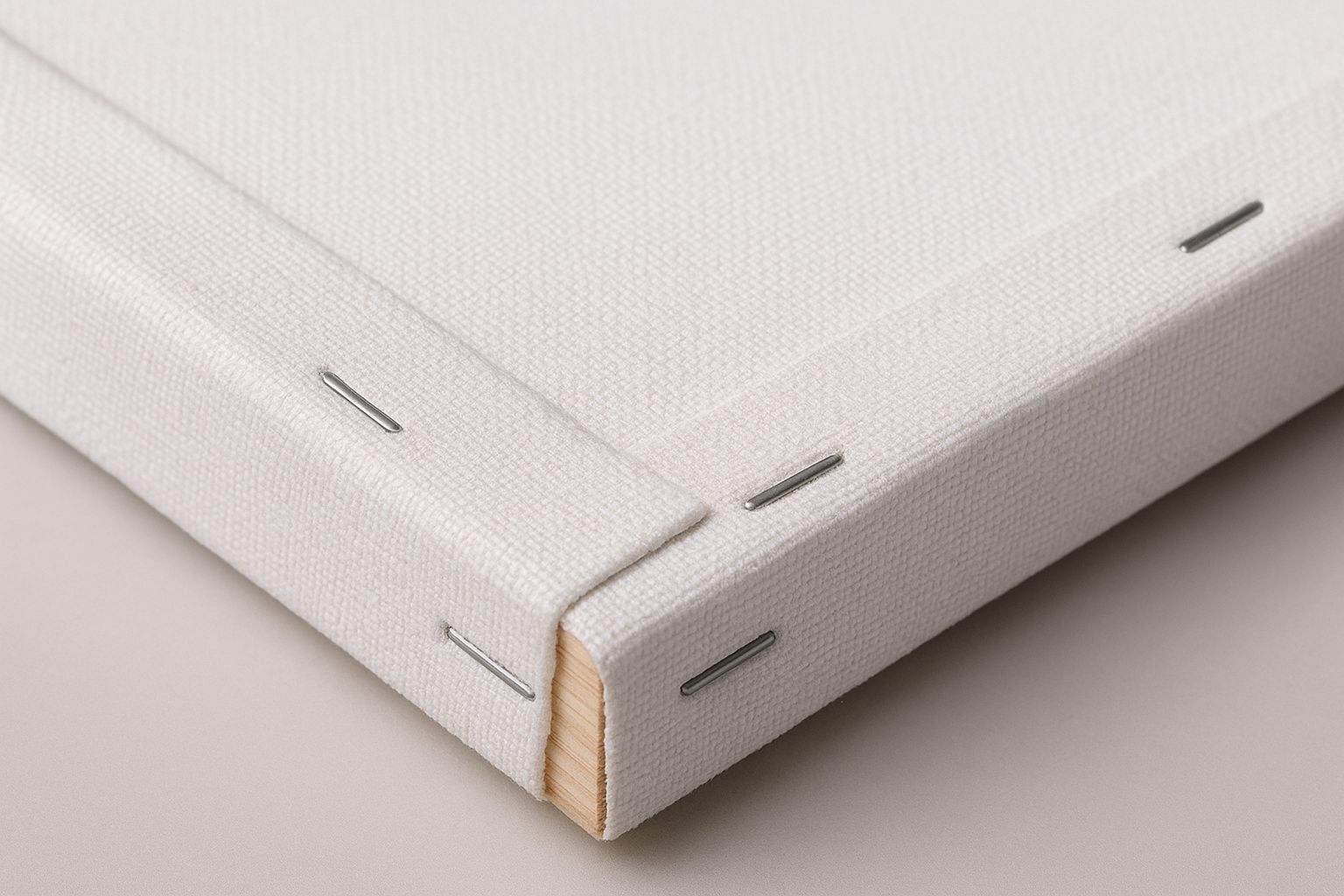 Close-up view of a white cotton canvas tightly stretched on a wooden frame showing fabric texture and corner detail.